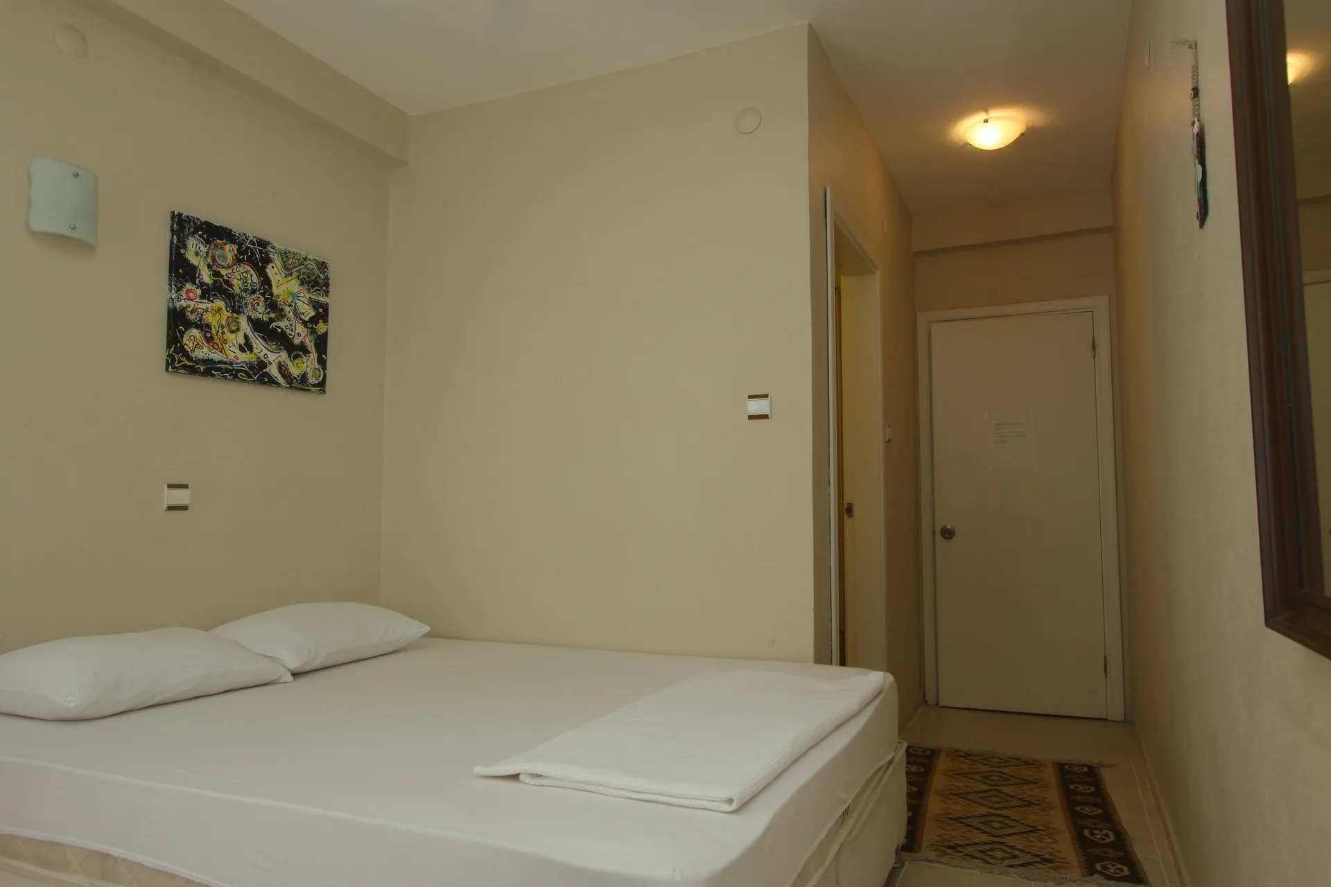 Neşe Otel Çeşme — çift kişilik oda, geniş yatak, tablo ve aydınlık koridor
